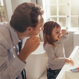 father and daughter brushing teeth in bathroom  