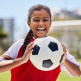 Child smiling while holding soccer ball on field