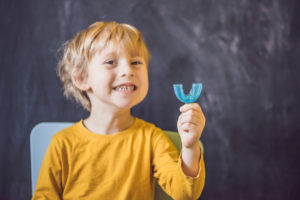 Young boy smiling and holding mouth guard