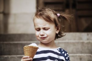 Frowning child with tooth sensitivity holding an ice cream cone