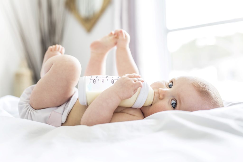 Baby drinking bottle while lying on bed