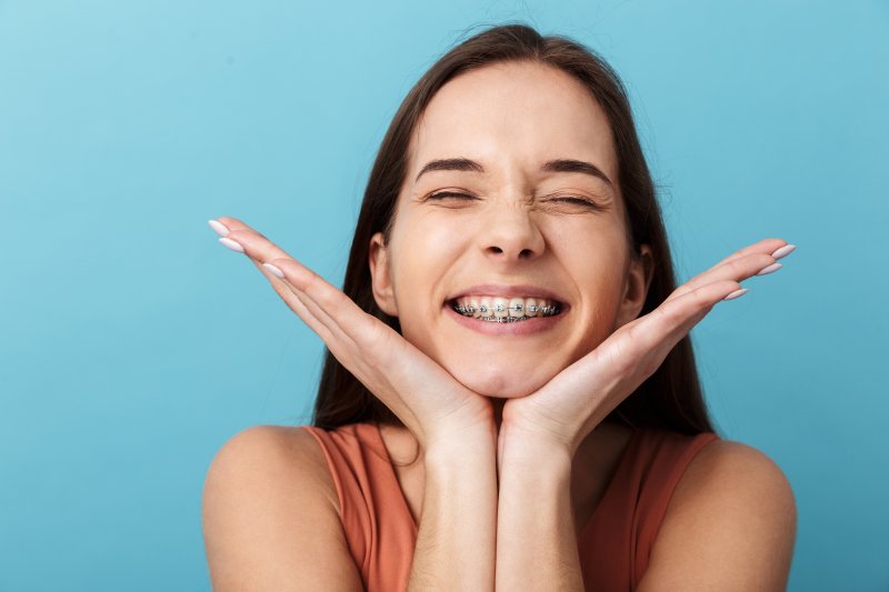 Young woman wearing braces smiling resting her chin in the palms of her hands as her fingers point outwards in a V-shape