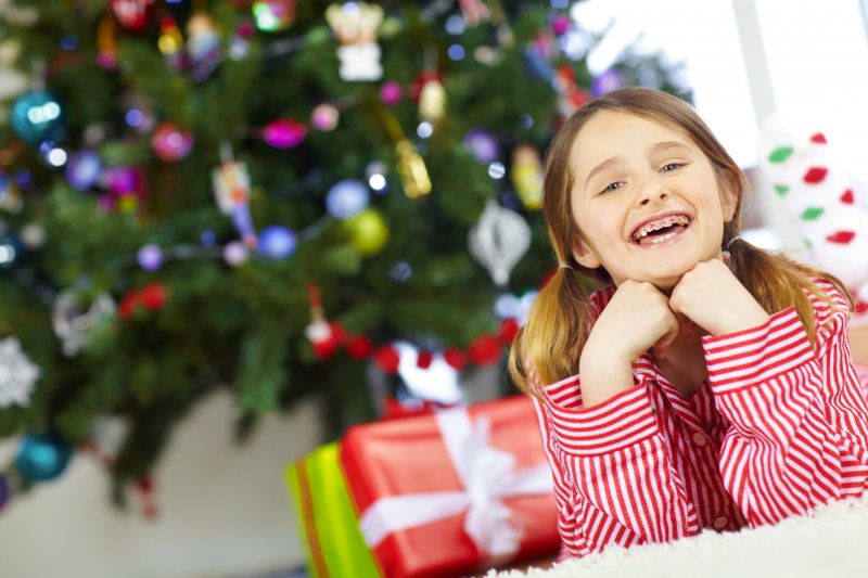 A child with braces smiling under a holiday tree